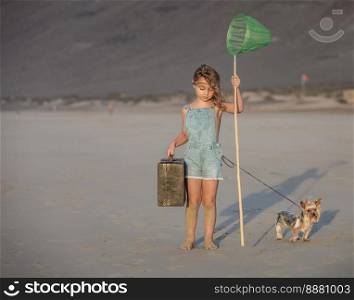 Full body barefoot girl with luggage and Yorkshire Terrier dog poking sand with scoop net while spending weekend day on Famara Beach in Lanzarote, Spain. Girl with suitcase and dog touching sand with scoop net