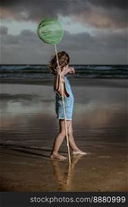 Full body barefoot girl with scoop net standing on wet sand and pointing at waving sea while spending stormy evening on Famara Beach in Lanzarote, Spain. Girl with scoop net pointing at sea