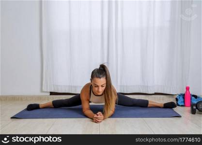 Full body of young flexible female in activewear performing Side Splits exercise while stretching legs during fitness workout at home. Fit woman stretching body in Side Splits pose