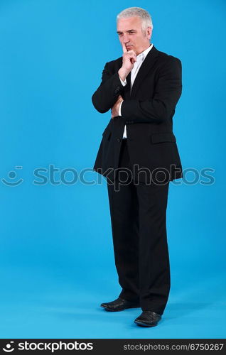 full-body portrait of mature pensive businessman holding finger before mouth