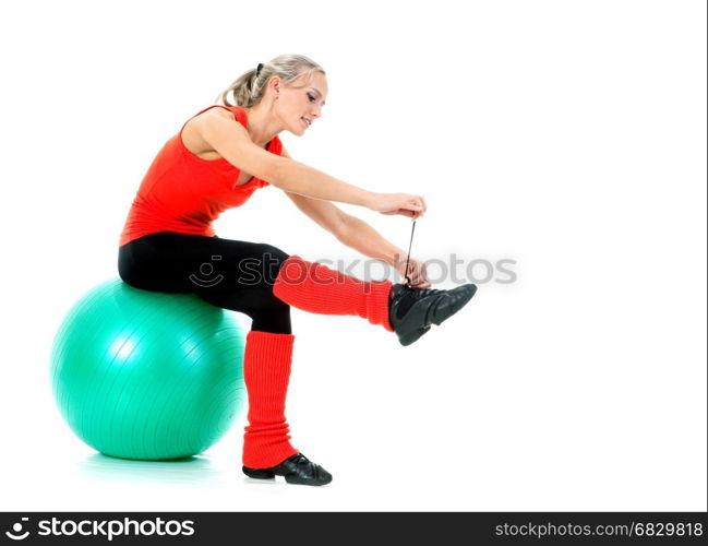 Full body shot of a woman sitting on the fitness ball and string together her sport shoe before training. Orange, green and black colors