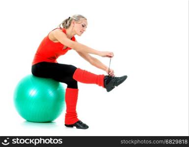 Full body shot of a woman sitting on the fitness ball and string together her sport shoe before training. Orange, green and black colors