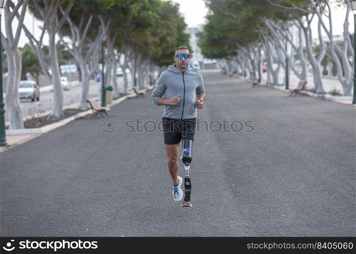 Full body strong mature male athlete with prosthetic leg jogging along asphalt path during cardio training on summer day in park. Handicapped sportsman running in park