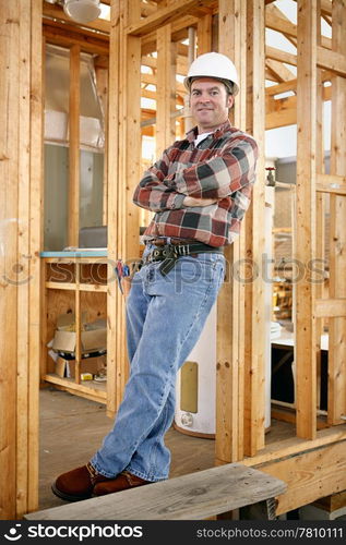 Full body view of a handsome construction worker leaning casually against a wood framed building. Authentic construction worker on actual construction site.