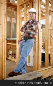 Full body view of a handsome construction worker leaning casually against a wood framed building. Authentic construction worker on actual construction site.