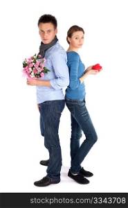 Full body young attractive couple standing back to back, woman holding heart, man holding flowers, isolated over white background