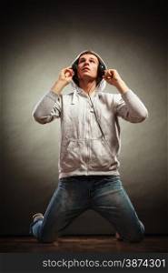 Full body young handsome man with headphones listening to music while kneeling looking up grunge background