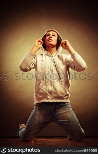 Full body young handsome man with headphones listening to music while kneeling looking up grunge background