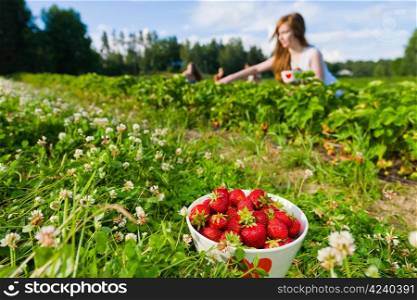 Full bowl of strawberries. Focus on bowl and group of girls behind, horizontal format