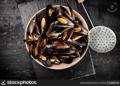 Full bowl with boiled mussels on a stone board. On a black background. High quality photo. Full bowl with boiled mussels on a stone board.