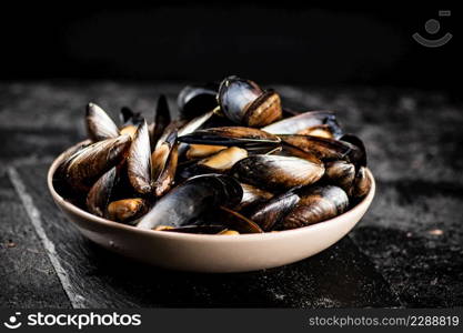 Full bowl with boiled mussels on a stone board. On a black background. High quality photo. Full bowl with boiled mussels on a stone board.