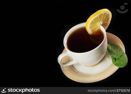 full cup of tea with lemon and greens leaves on black