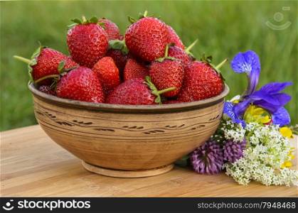 Full earthenware bowl of delicious strawberries with a bouquet of wildflowers. Full earthenware bowl of delicious strawberries
