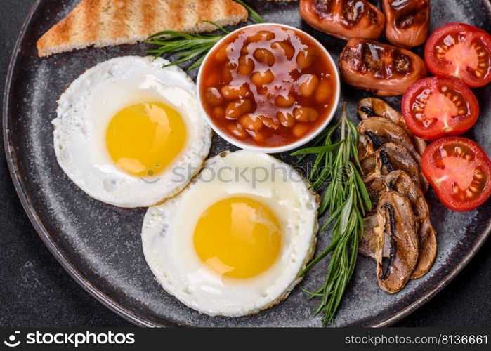 Full english breakfast - bean, fried eggs, roasted sausages, tomatoes, mushrooms on a dark concrete table with toasted bread. Full english breakfast with bean, fried eggs, roasted sausages, tomatoes and mushrooms