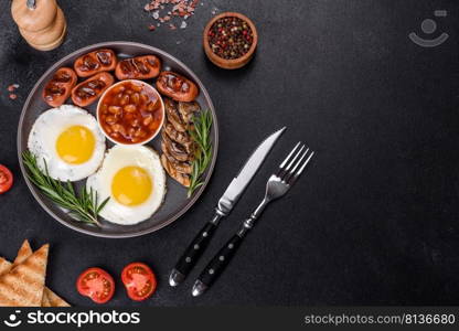 Full english breakfast - bean, fried eggs, roasted sausages, tomatoes, mushrooms on a dark concrete table with toasted bread. Full english breakfast with bean, fried eggs, roasted sausages, tomatoes and mushrooms