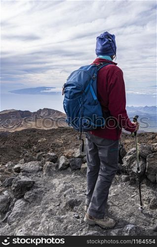 full equipped senior hiker standing on a rocky mountain path with scenic view