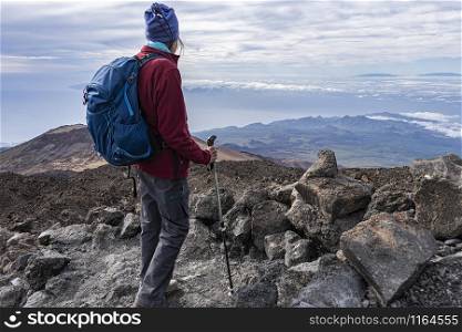full equipped senior hiker standing on a rocky mountain top with scenic view