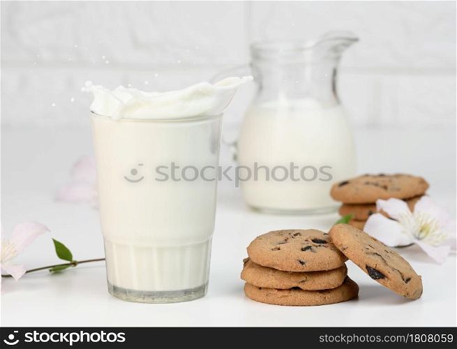 full glass cup of fresh milk with splashes stands on a white table, healthy breakfast