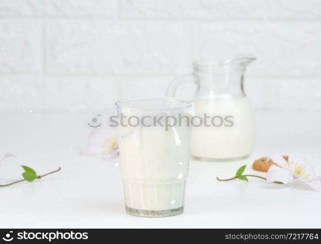 full glass cup of fresh milk with splashes stands on a white table, healthy breakfast