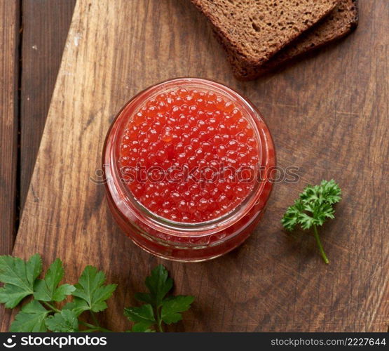 full glass jar with red caviar on a brown wooden table, top view