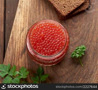 full glass jar with red caviar on a brown wooden table, top view