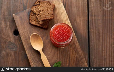 full glass jar with red caviar on a brown wooden table, top view