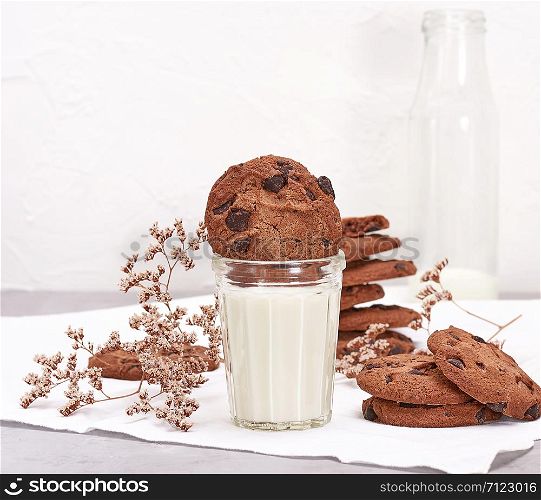 full glass of milk and round chocolate chip cookies, an empty milk bottle behind