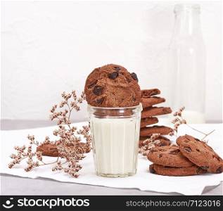 full glass of milk and round chocolate chip cookies, an empty milk bottle behind