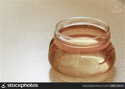 full honey pot glass, jar of organic floral honey or syrup on table