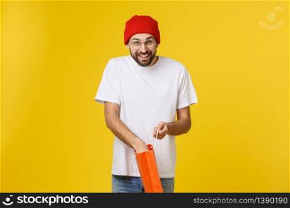 Full isolated studio picture from a young man opening shopping bags. Isolate over yellow background. Full isolated studio picture from a young man opening shopping bags. Isolate over yellow background.