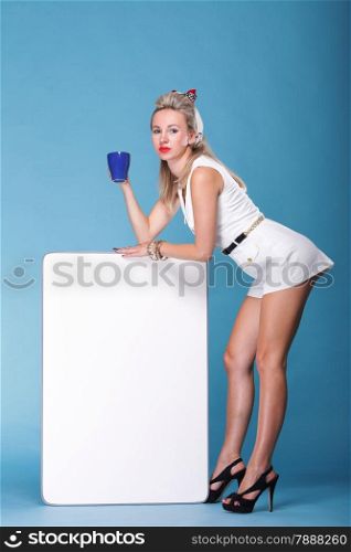 full lenght Beautiful young woman with pin-up make-up and hairstyle posing in studio with white board cup of tea
