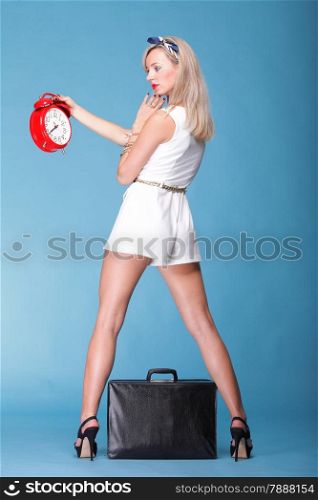 full lenght Portrait of pretty young woman in white dress and black travel bag against blue background timer red clock