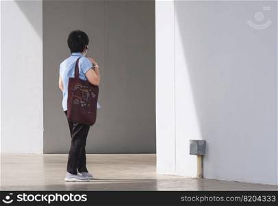 Full length and rear side view of Asian woman carrying reusable brown canvas eco friendly tote bag is walking into supermarket