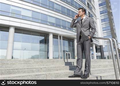 Full length businessman answering cell phone while standing on steps outside office