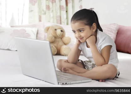 Full length cute girl looking at laptop in bed