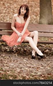 Full length fashionable young woman in red dress outdoor relaxing in park sitting on bench vintage photo sepia tone