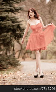 Full length fashionable young woman in red dress outdoor relaxing walking in park vintage photo sepia tone