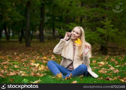 Full length, happy blonde woman calling by phone in autumn park
