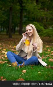 Full length, happy blonde woman calling by phone in autumn park