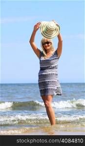 Full length mature woman with hat on beach enjoying summer holiday