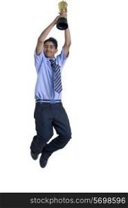 Full length of a boy jumping in air with trophy against white background
