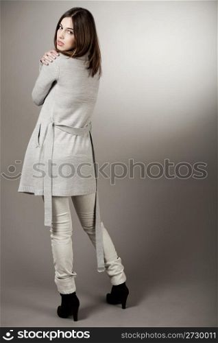 Full length of a model turning back with her spring coat on a light background