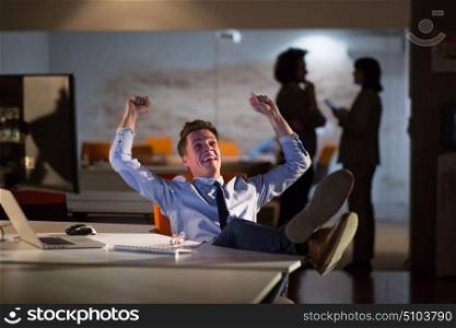 Full length of a relaxed casual young businessman sitting with legs on desk at night office