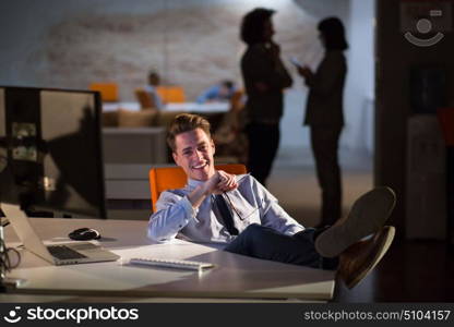 Full length of a relaxed casual young businessman sitting with legs on desk at night office