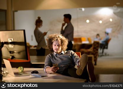 Full length of a relaxed casual young businessman sitting with legs on desk at night office