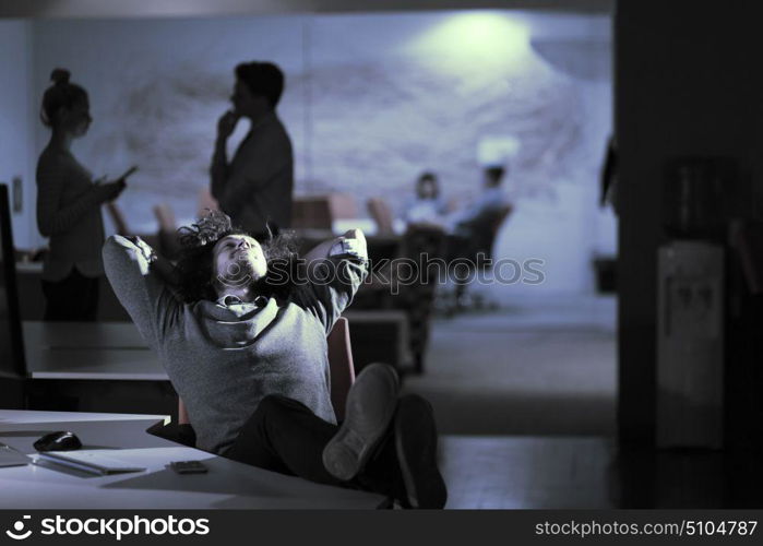 Full length of a relaxed casual young businessman sitting with legs on desk at night office