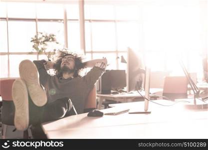 Full length of a relaxed casual young businessman sitting with legs on desk at office