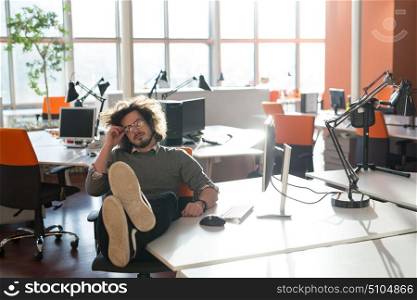 Full length of a relaxed casual young businessman sitting with legs on desk at office