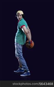 Full length of a young man holding basket ball behind his back against black background