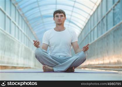 Full length of a young man meditating in lotus position outdoors at bridge